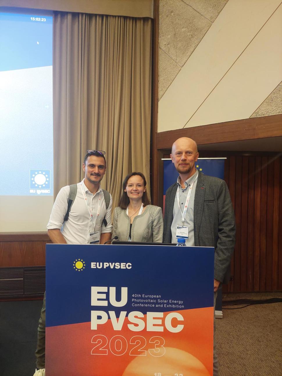 trzy osoby nad szyldem z konferencji