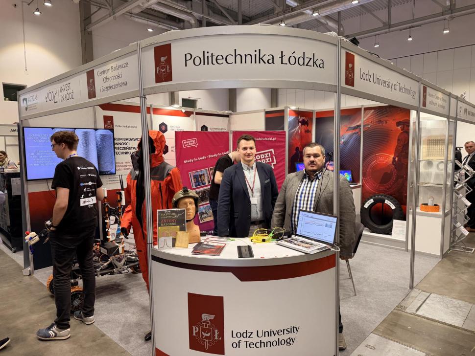 Pracownicy katedry na stanowisku uczelni podczas targów AZYL EXPO 2026, przedstawiający rozwiązania czujników światłowodowych.